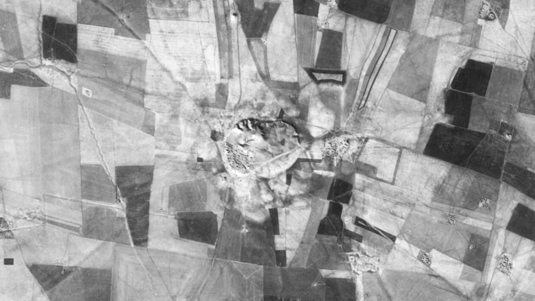 Black and White satellite image of a flat landscape with an elevated formation near the centre of the image