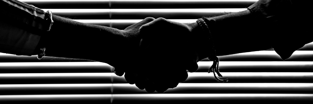 monochrome photo of people shaking hands in front of a horizontal blind