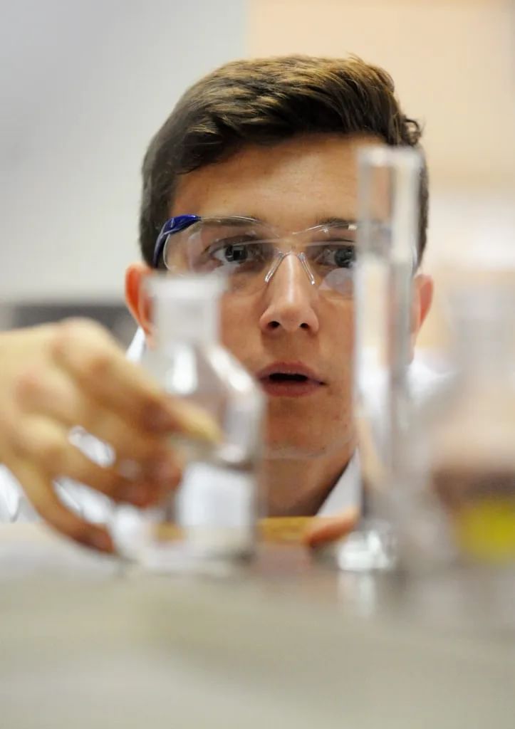 A student in safely specs clasps a glass test tube and bottle