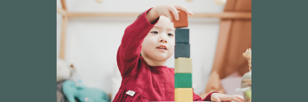 A child in a red shirt stacks colorful blocks in a tower