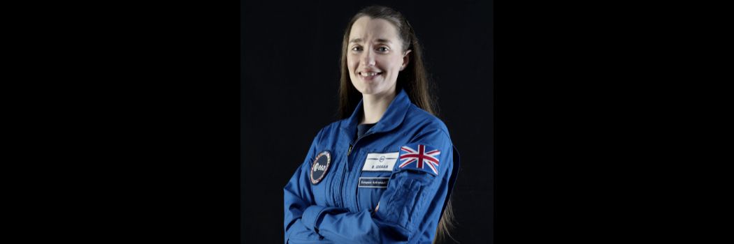 Rosemary Coogan standing with arms folded in a blue astronaut's boiler suit with a Union Flag on the sleeve.