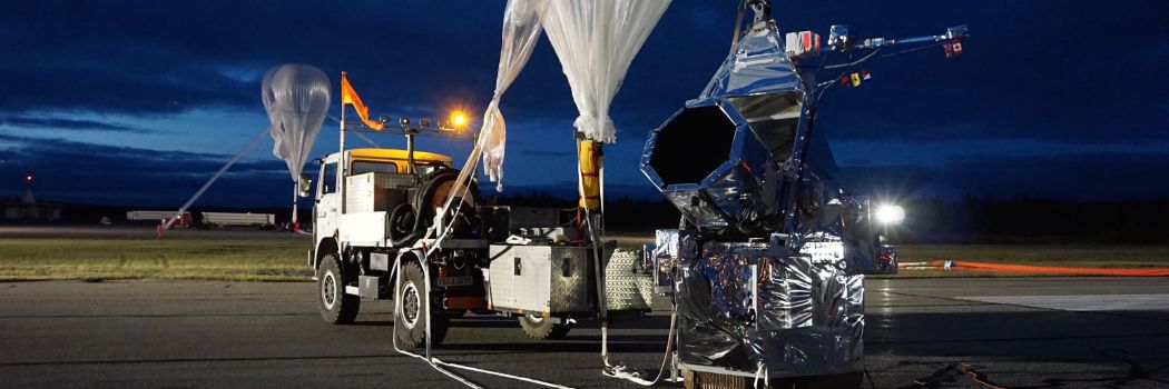 A silver clad telescope sits on the runway at dawn with a truck and giant helium balloon in the background