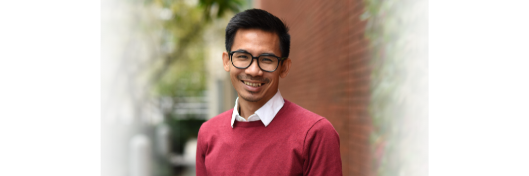 A picture of Dr Aung Hein smiling at the camera. He is wearing a red sweater.