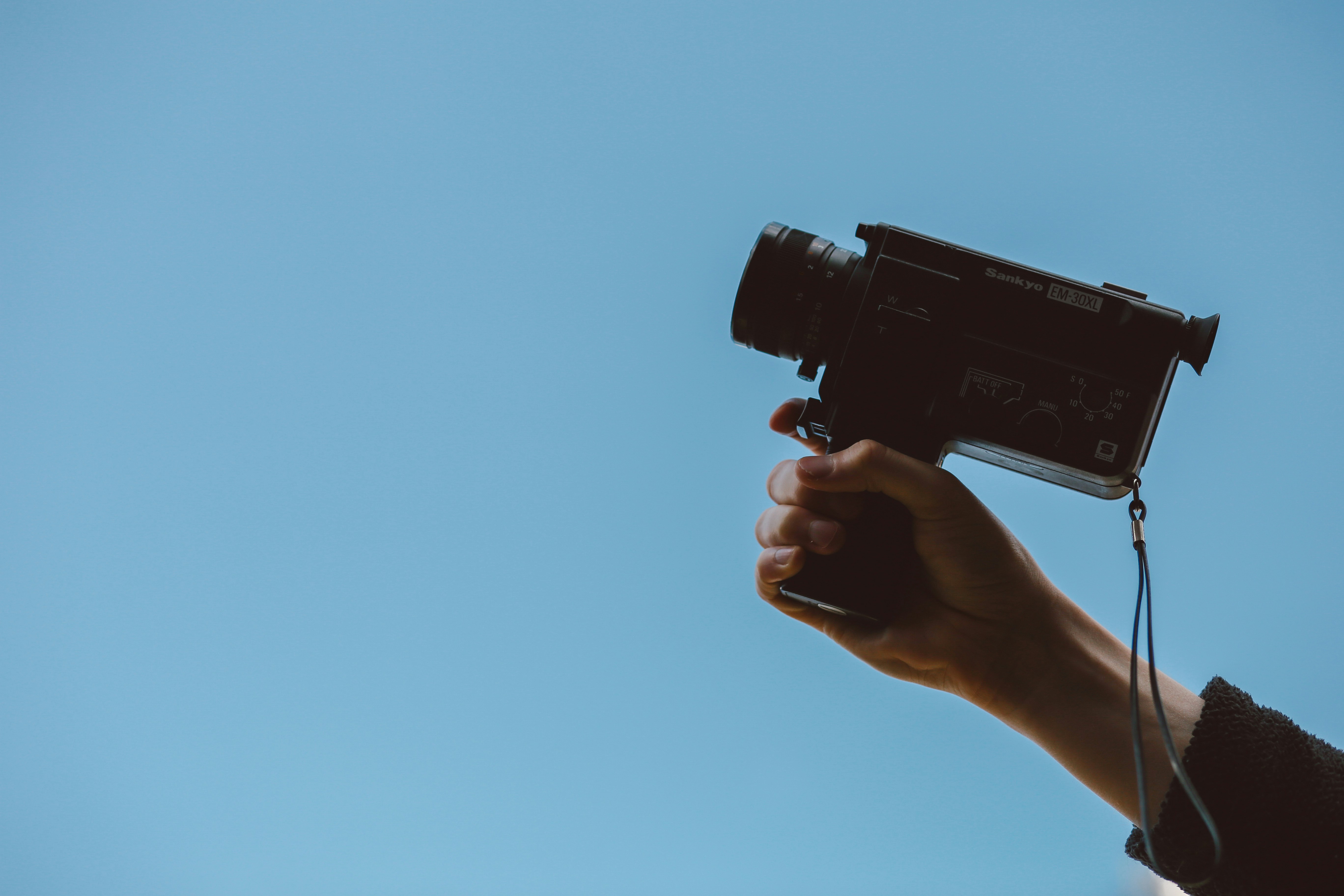 Hand holding film camera aloft against a blue sky.