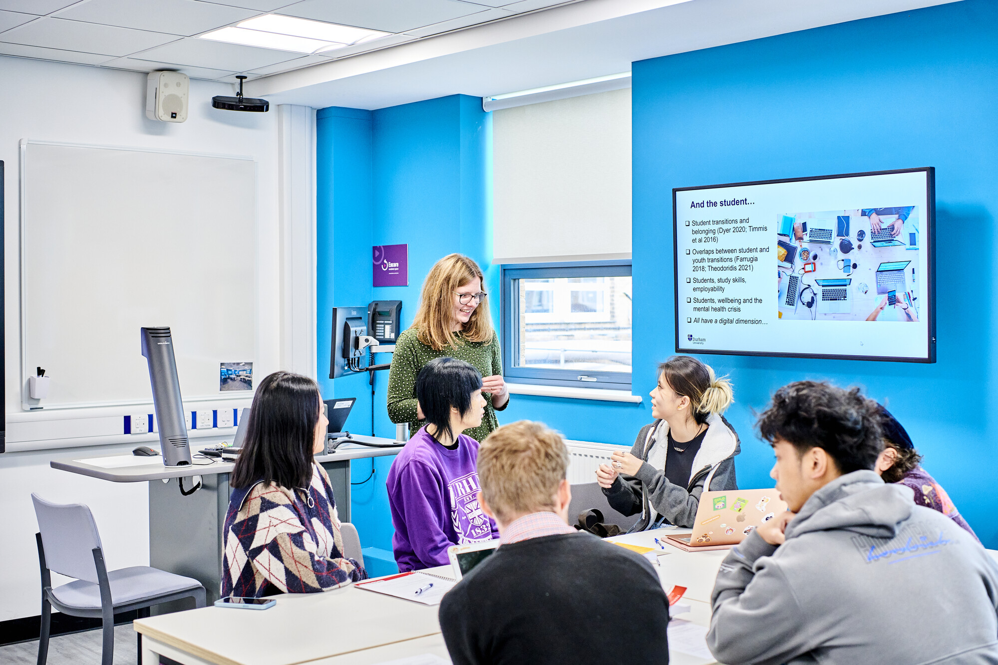 TAcademic in green dress discussing research with students who are sat at a table