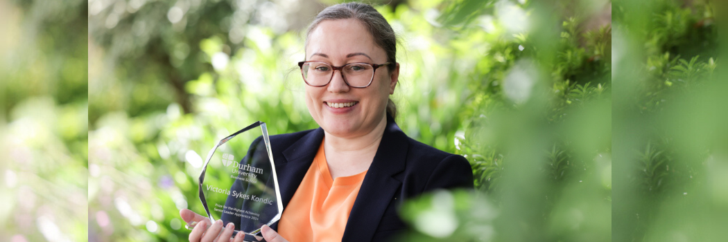 Woman holding a glass award in the sunshine next to a green tree