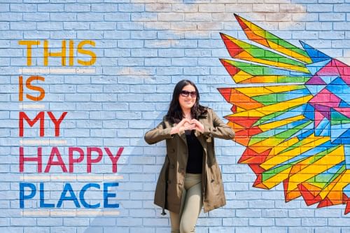 Student making a hand heart in front of mural saying 