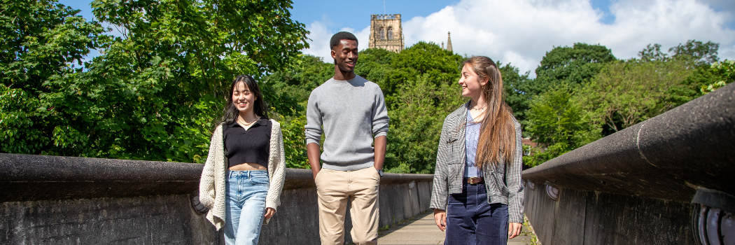 Three students walking over a bridge in Durham. Cathedral in view behind them