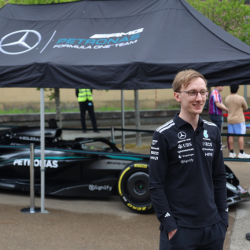 Alumnus Harry Brooks in black overall and wearing glasses in front of a Formula One car