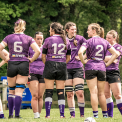 six women in purple Durham rugby shirts and black shorts on a rugby field
