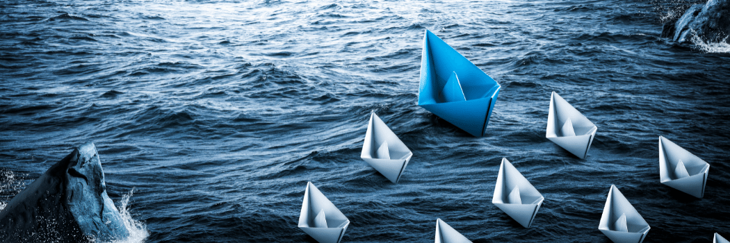A blue paper sailing boat on water followed by smaller white paper boats