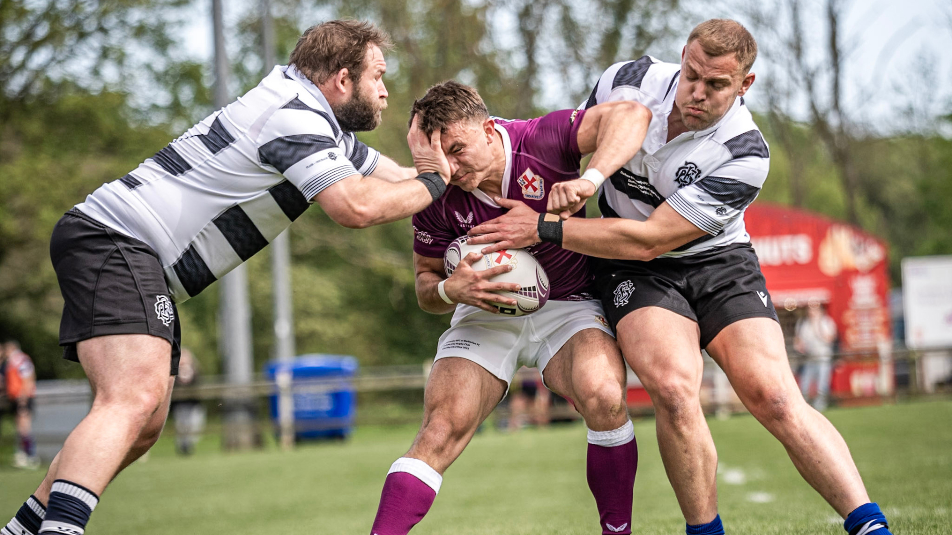 Two teams of rugby players wearing purple tops, and black and white tops, playing against each other