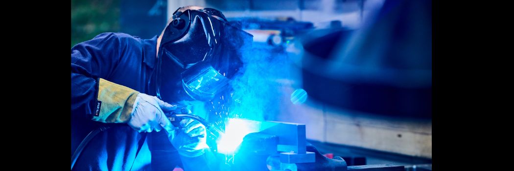 Person wearing protective facemask welding, with bright blue flame visible