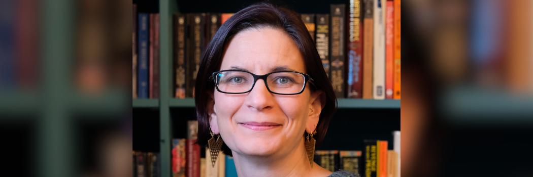 Professor Leah Morabito smiling to camera with bookshelves behind her