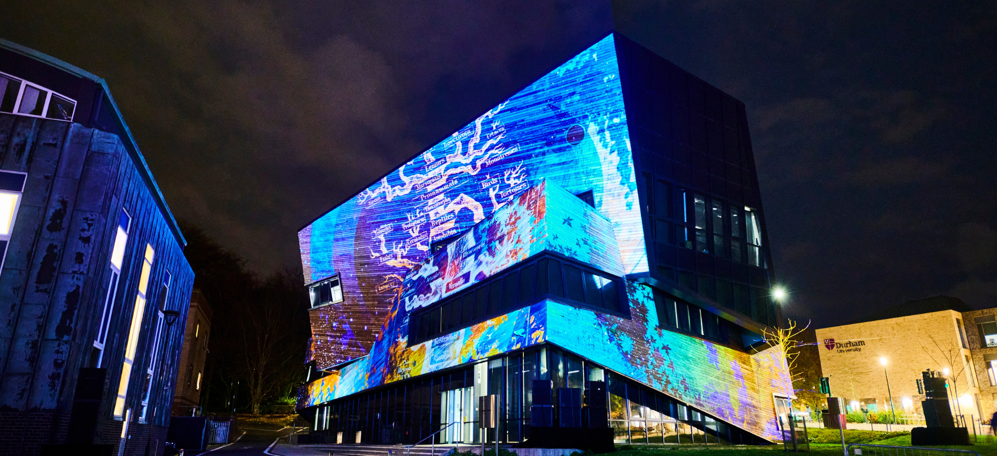 Night time image from Lumiere 2021 showing the Ogden building with colourful abstract images projected onto one side