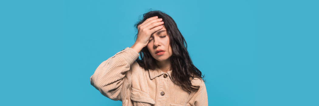 A woman with her hand against her forehead and a pained expression.
