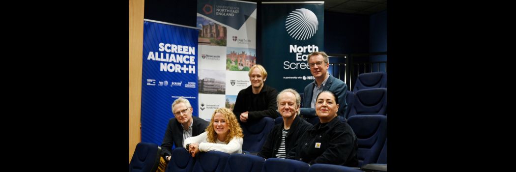 Six people sitting in a theatre, backed by pull-up banners