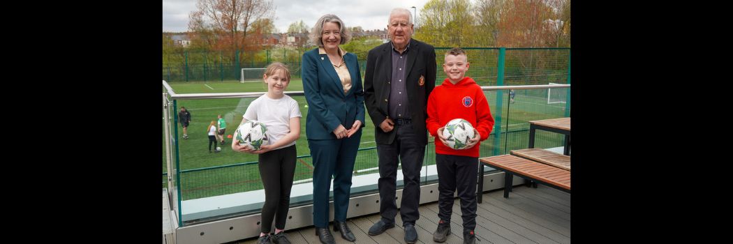 A girl, a woman, a man, and a boy standing, the children holding footballs