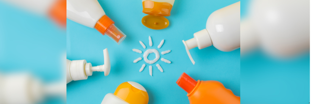 Sunscreen bottles arranged in a circle around a sun drawn in white cream on a bright blue background