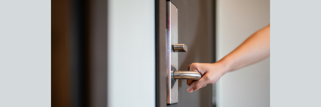 A close up of a person's hand holding a silver door handle.