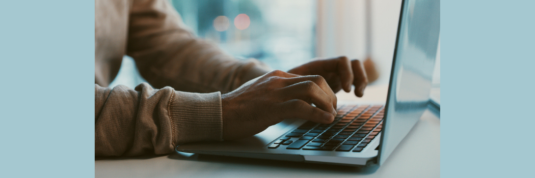 A close-up of a man's hands typing on a silver laptop with black buttons.