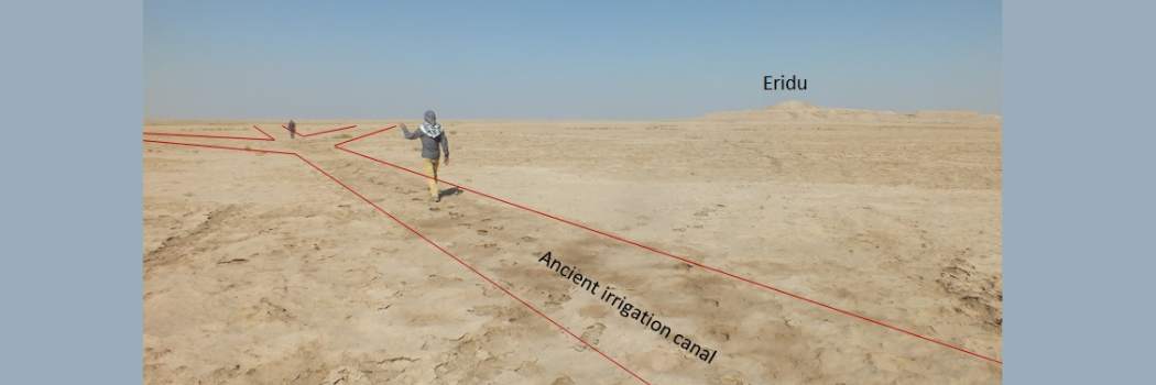 A desert landscape with a faint channel running through it and a person walking along it