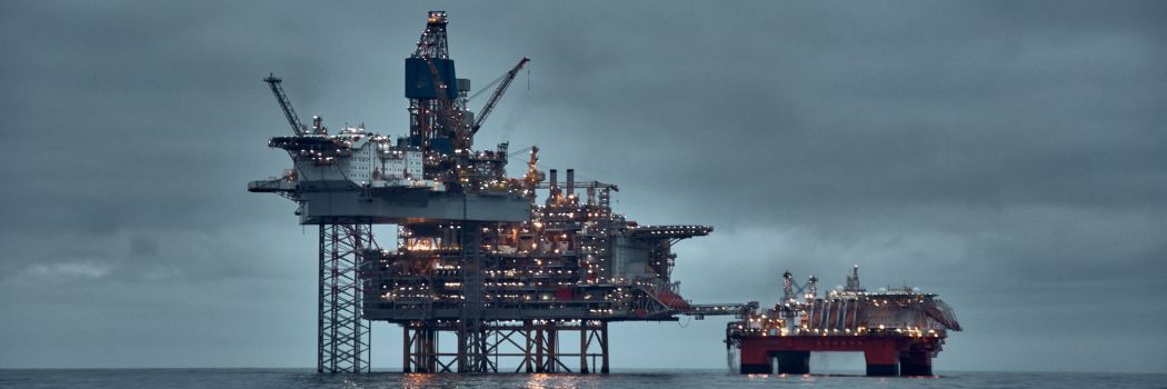 An offshore oil and gas rig stands in the sea against a cloudy and dark skyline.