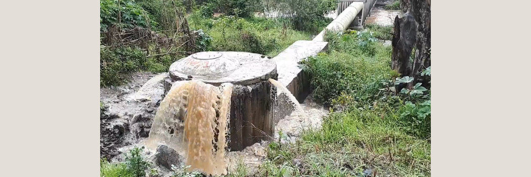 A water pipe outdoors with dirty brown water overflowing from it.