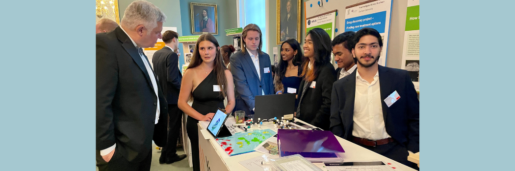 A group of students in formal attire talking with a man in a hall.