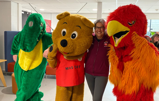Crocodile, bear and parrot mascots posing with student