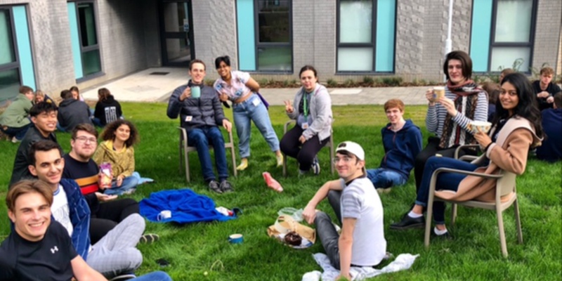 A group of students sitting in the grass having tea and cake