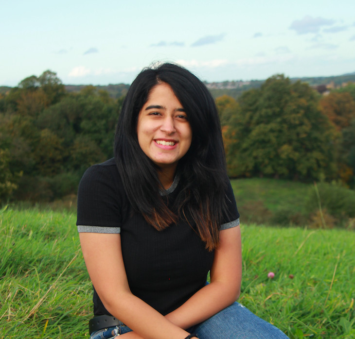 A student sitting on grass with trees in the background