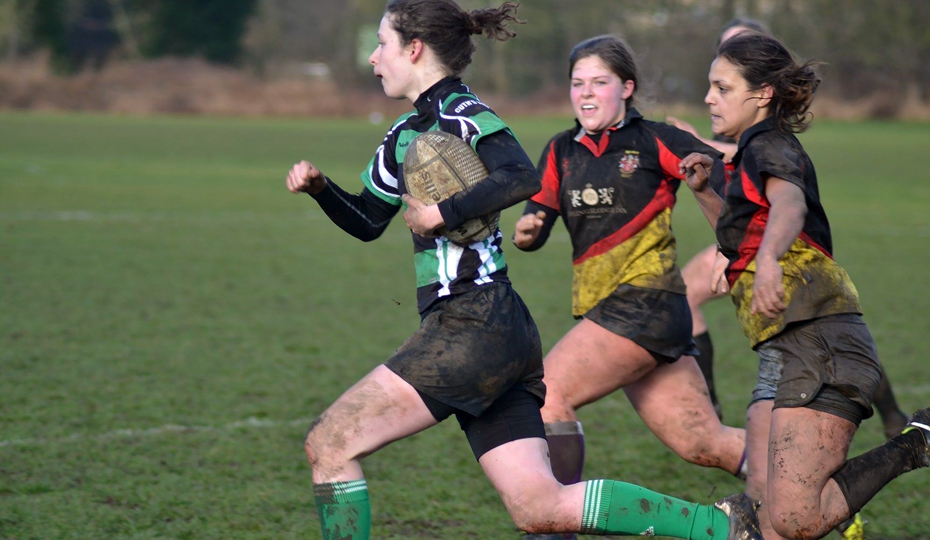 Cuth’s female rugby player in green kit running with a rugby ball and being chased by 2 opponents.