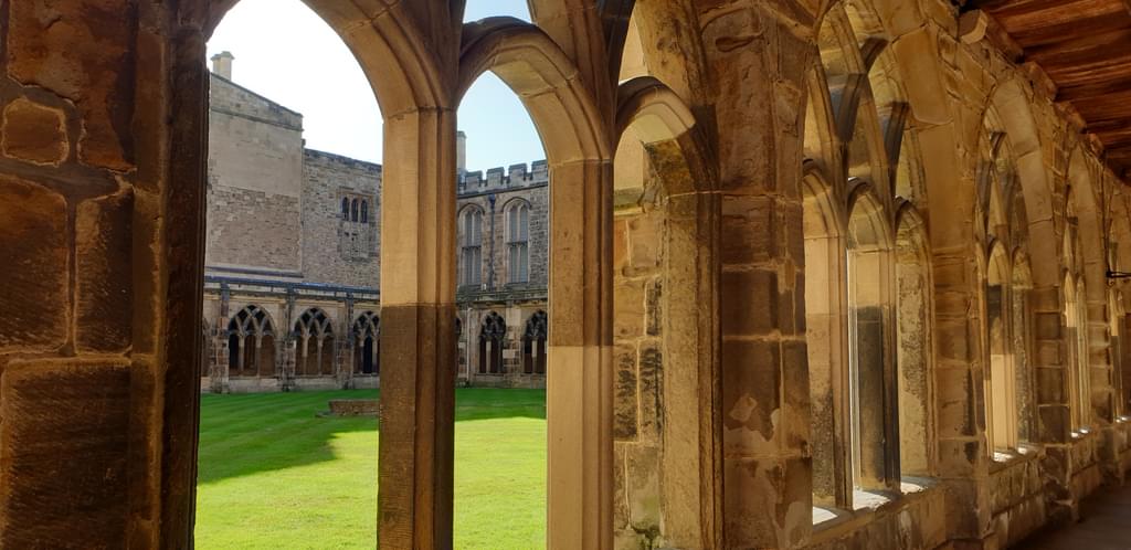 Photo of Durham Cathedral cloisters with a sunlit grassy lawn visible between the arched columns.