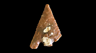 A flint barb and tanged Early Bronze Age arrowhead on a black background