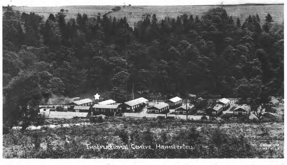 Black and white photograph of a camp comprising huts within a forest