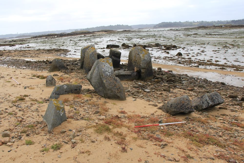 Large stones of a Neolithic tomb in sand in the foreground with the sea behind