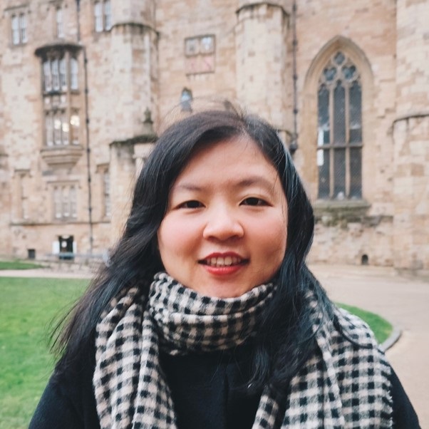 A lady with long dark hair, smiling wearing  black coat and checked black and white scarf