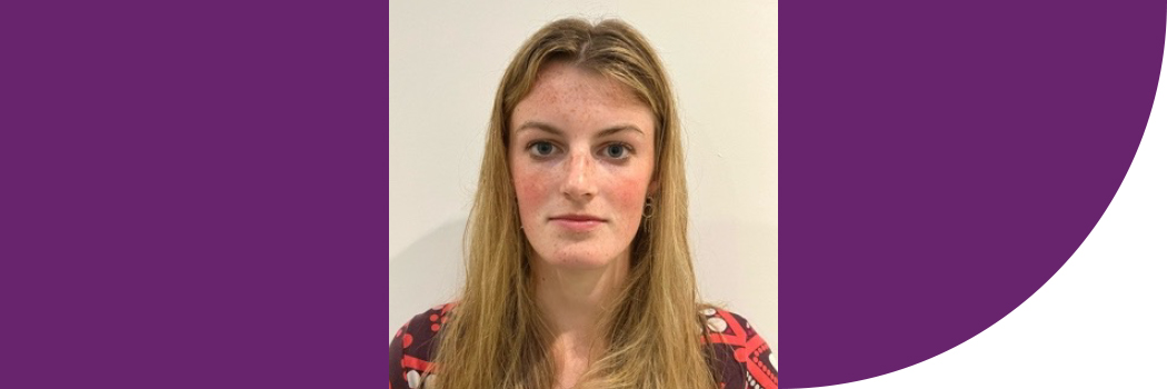 Female student, with blonde hair, stood against white wall