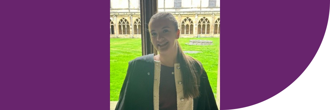 Female student with brown hair, wearing academic gown, in cathedral.