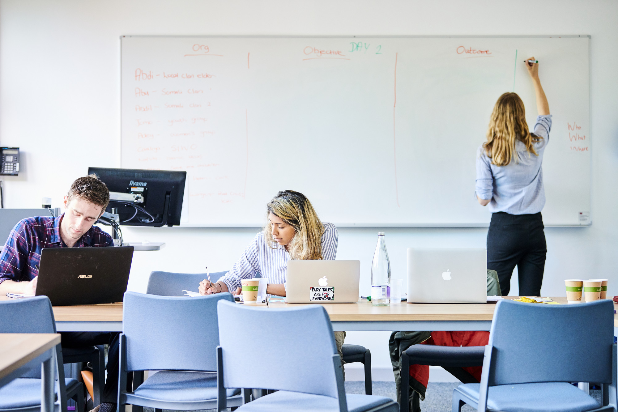 Tutor writing on a whiteboard with two students taking notes