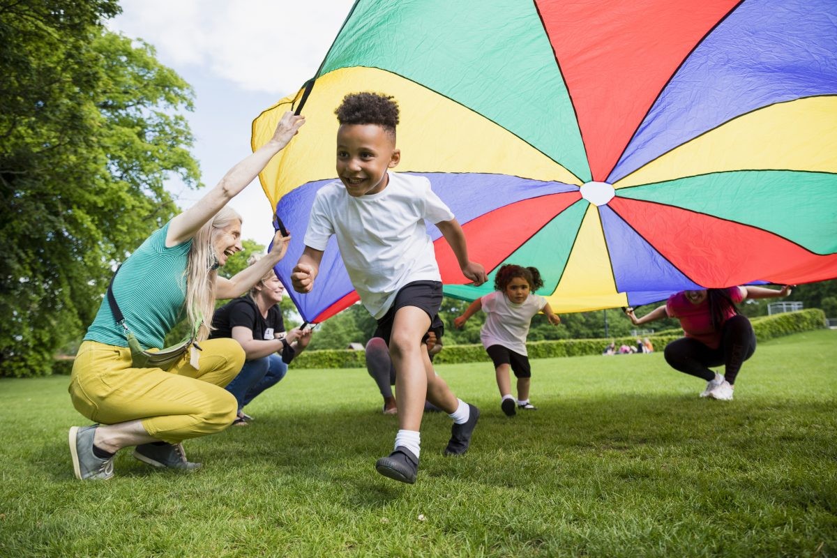 A young child running underneath a colourful parachute as part of play time.