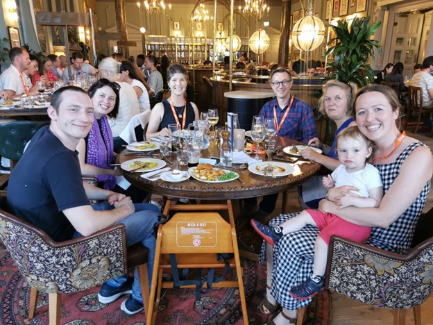 A group of men and women posing for a photograph sat at a dinner table in a restaurant