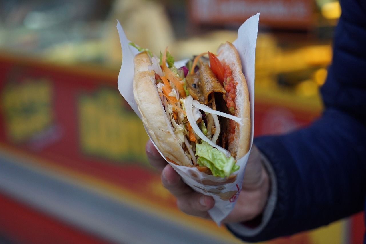 A man's hand holding a takeaway kebab wrapped in paper
