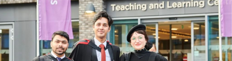 Students in graduation gowns and a guest outside the teaching and Learning Centre