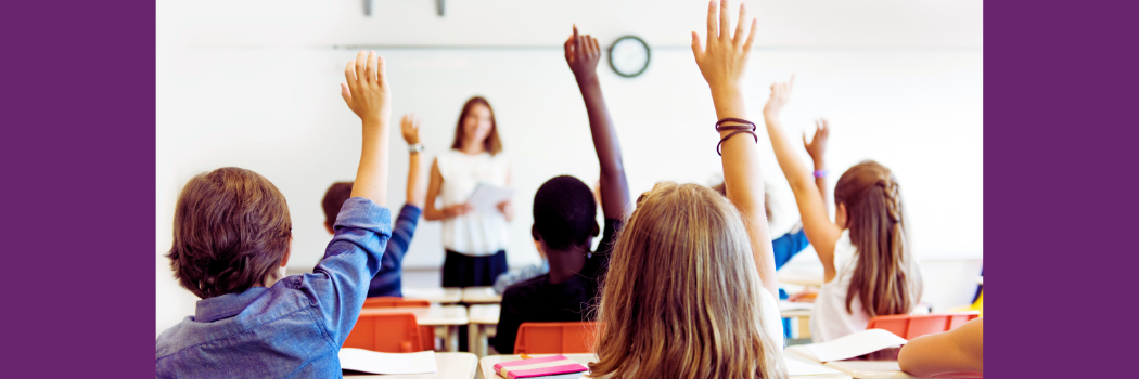 Children sitting in a classroom raise their hands