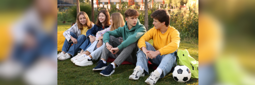Five teenage children sat together on grass in conversation