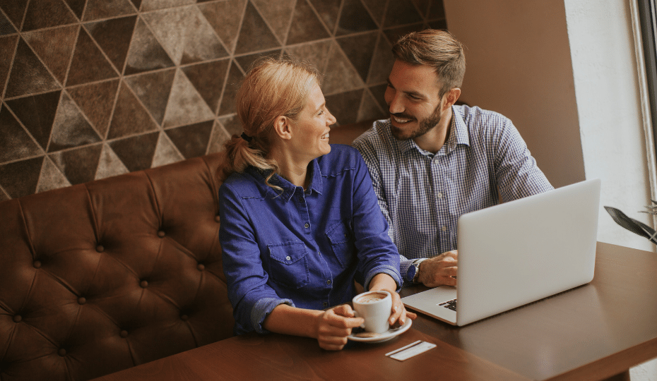 A couple with a laptop with the woman holding a cup of coffee