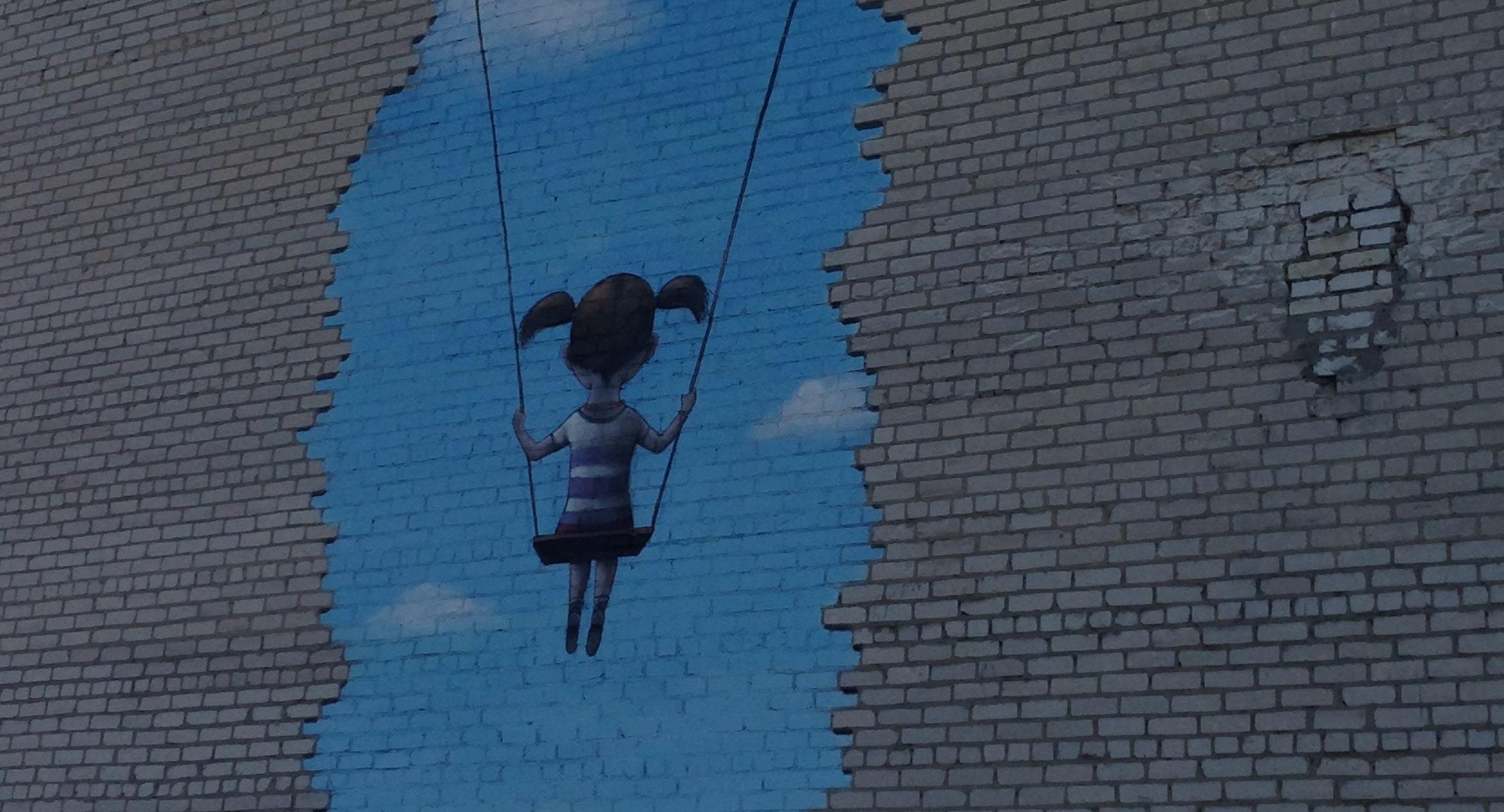 A repaired brick wall with a painted picture of a girl on a swing