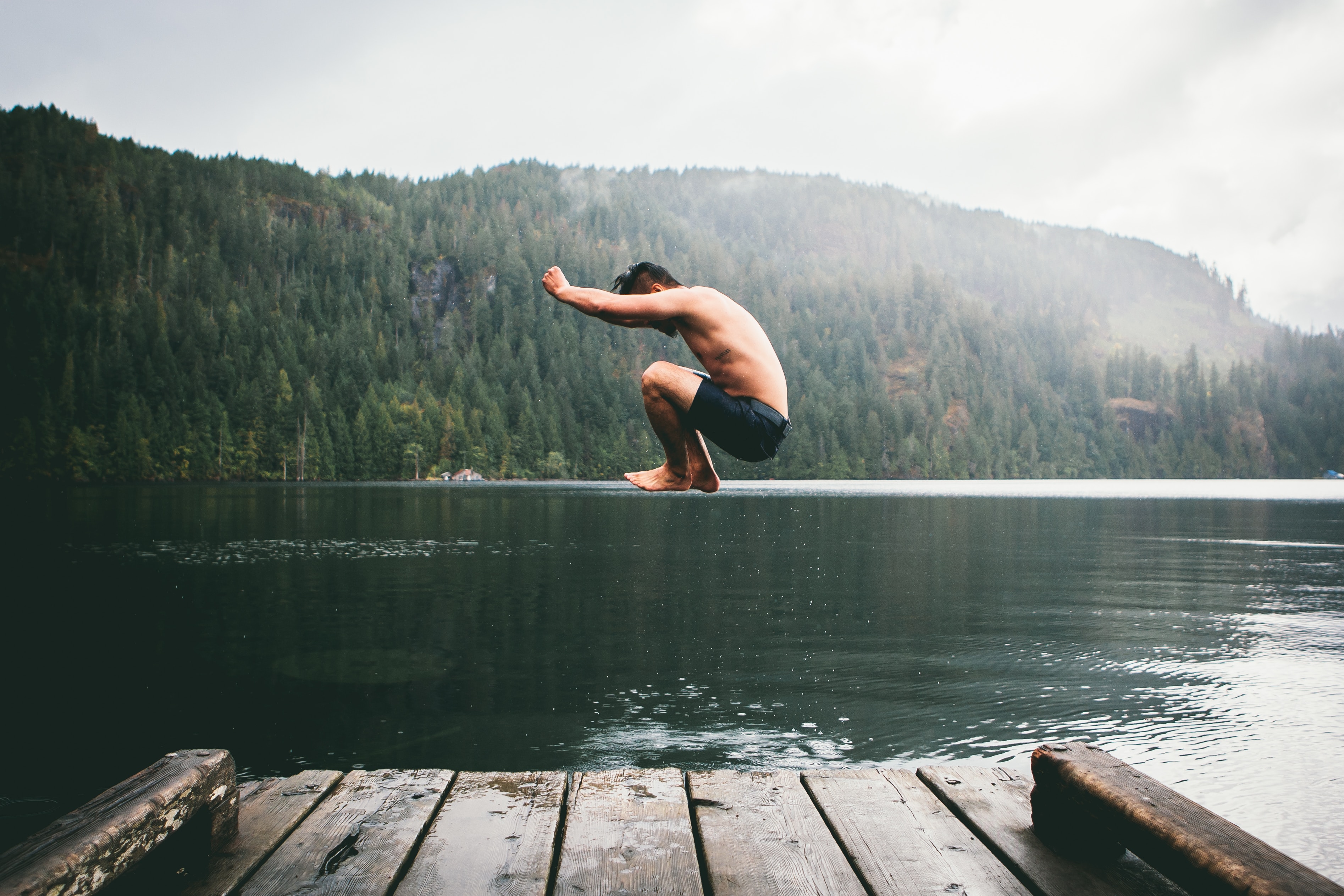 A white man in border shorts jumping into a river